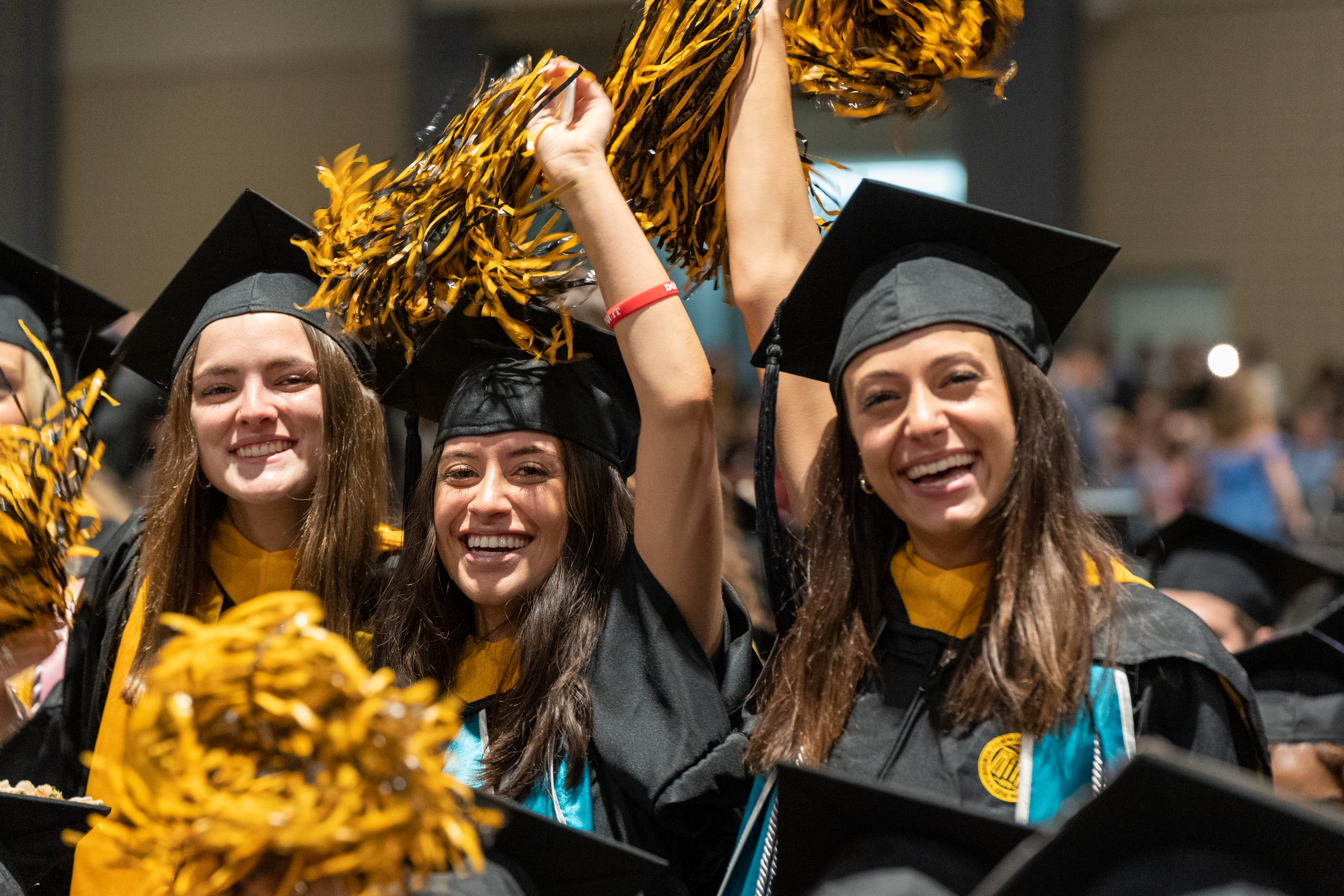 Three female graduates in cap and gown celebrating with pom-poms