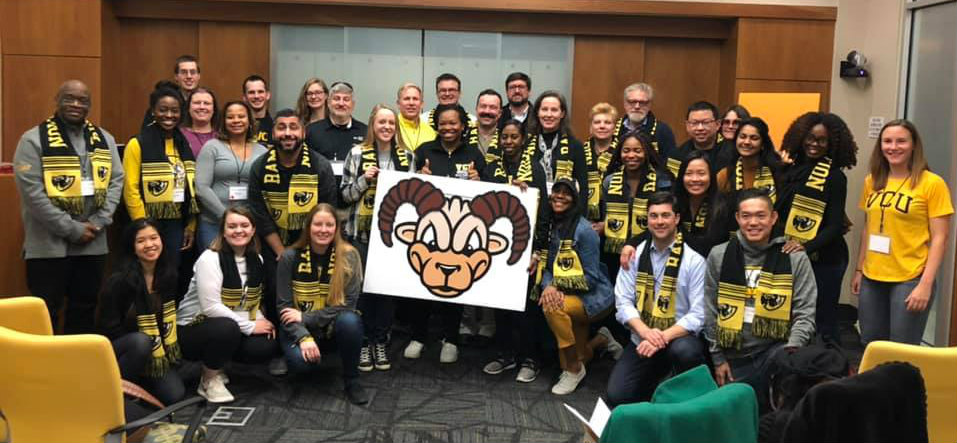 Group of volunteers wearing black and gold and holding an image of Rodney the Ra